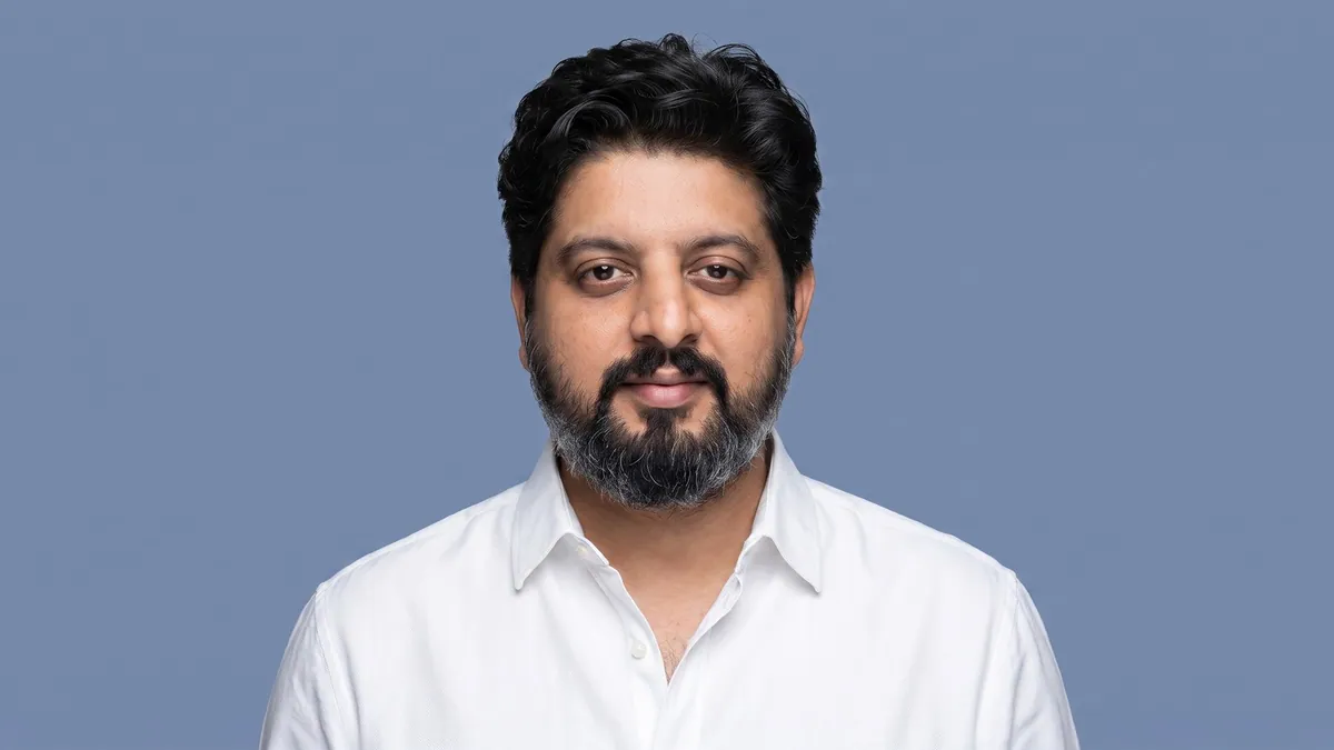 Portrait of Abhishek Mehta in a white shirt against a flat pastel slate blue backdrop