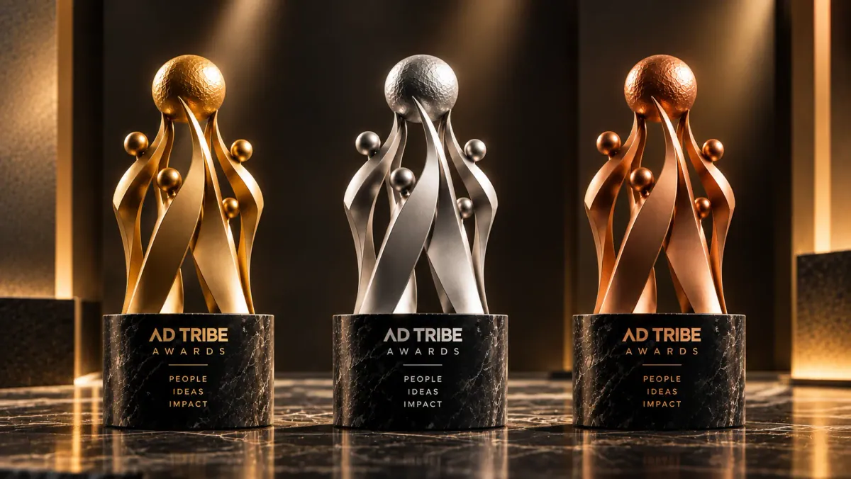 Three Ad Tribe Awards trophies in gold, silver and bronze on black marble bases, lit against a dark stage backdrop