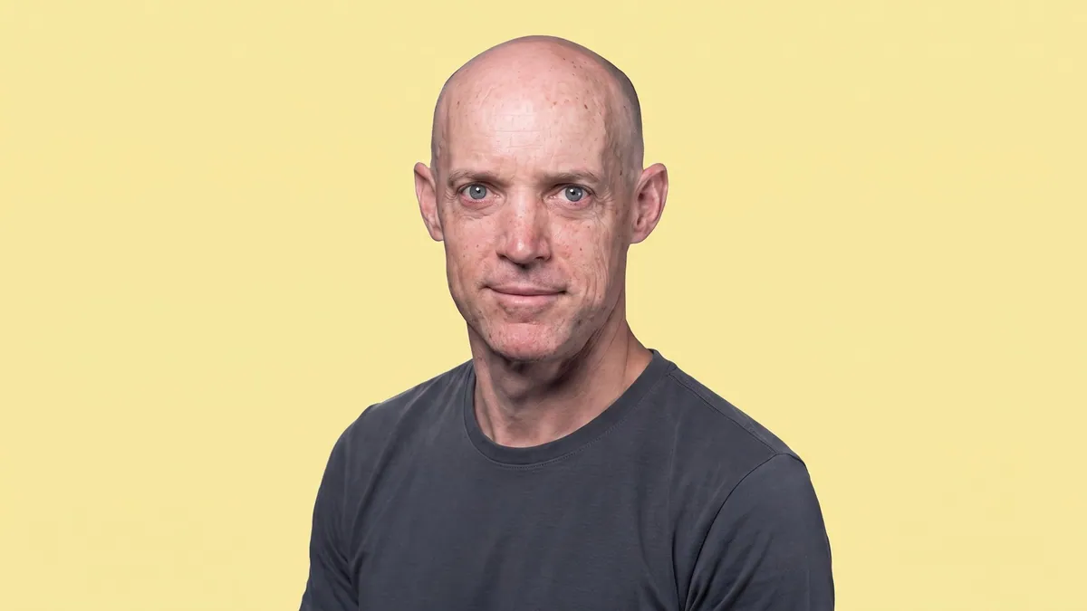 Portrait of Anthony Armstrong in a dark grey t-shirt against a flat pastel butter yellow backdrop