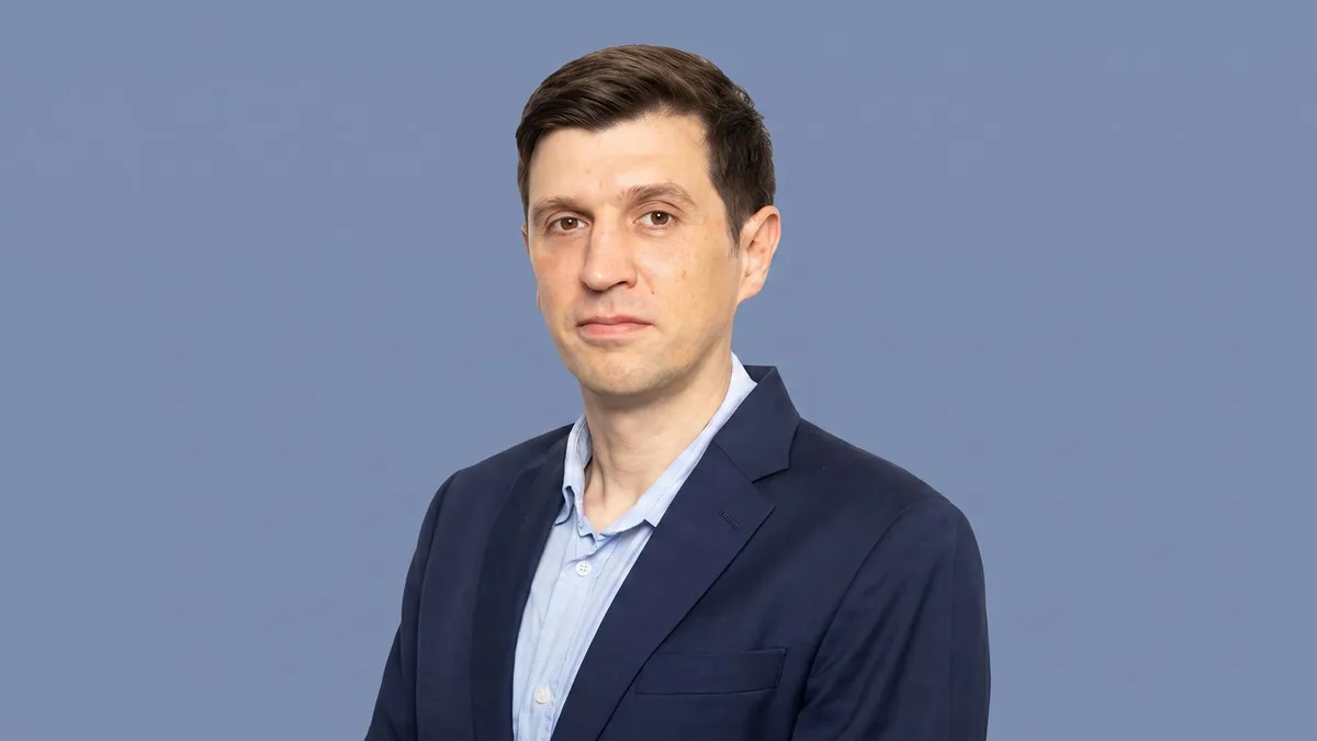 Jon Russell, executive director at Ellerton and Co, photographed against a flat slate blue background