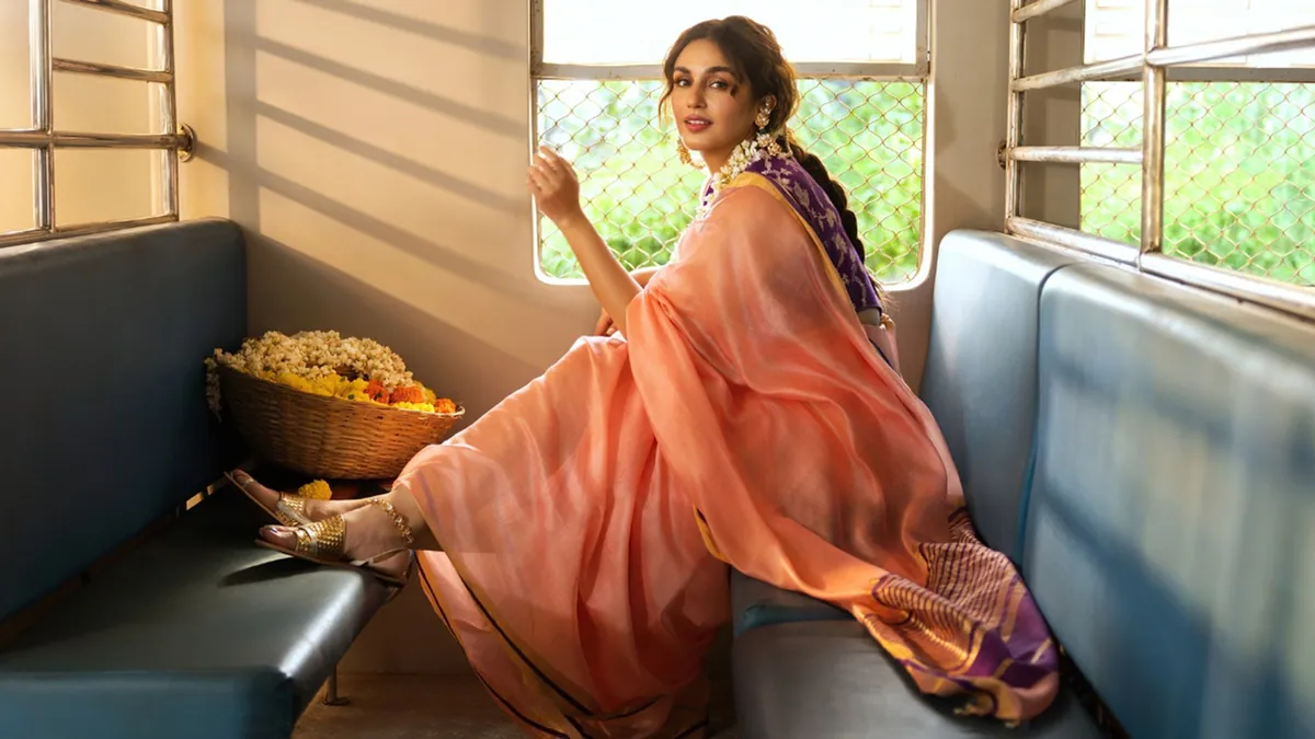 Huma Qureshi in a peach handwoven Freefall saree, seated by a train window