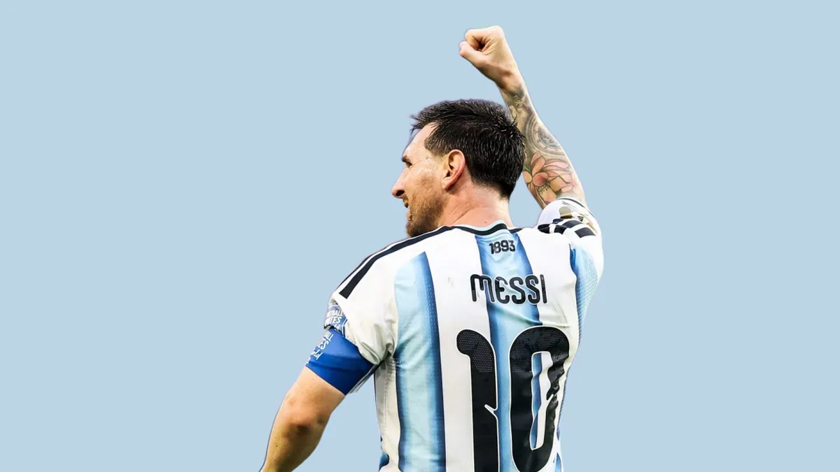 Lionel Messi celebrating with a raised fist, seen from behind in the Argentina number 10 shirt, against a flat powder blue background