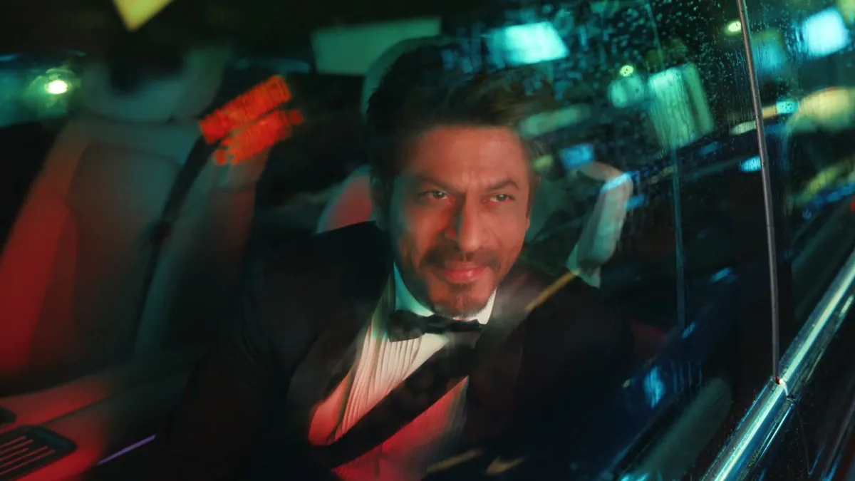 Shah Rukh Khan in a tuxedo in the back of a car at night, in a frame from the Vi teaser film