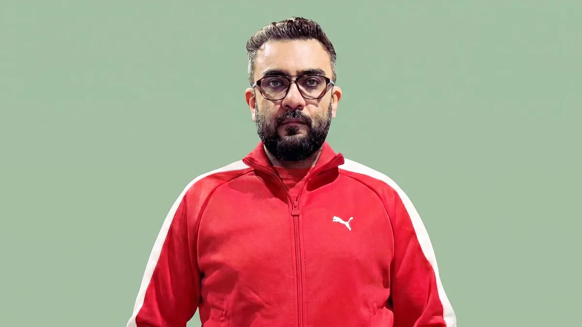 Portrait of Vishal Arora in a red Puma track jacket against a flat pastel sage green backdrop