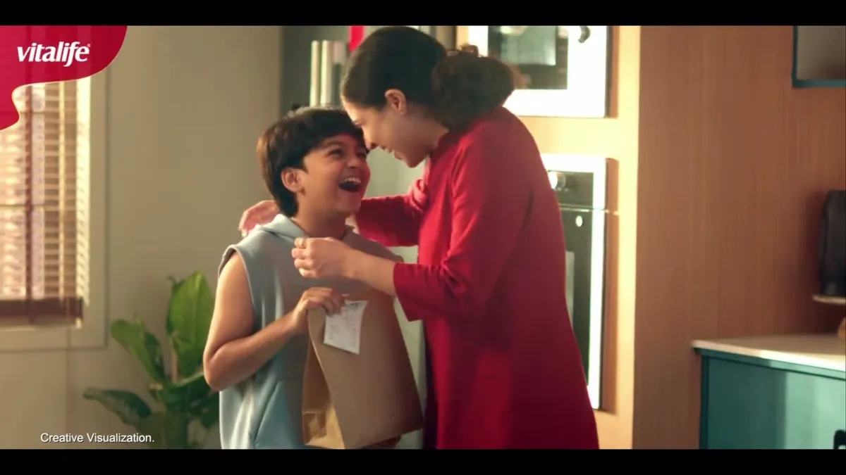 A mother greeting her son as he carries home a paper takeaway bag, from Vitalife's Swaad Swaad Mein Sehat film